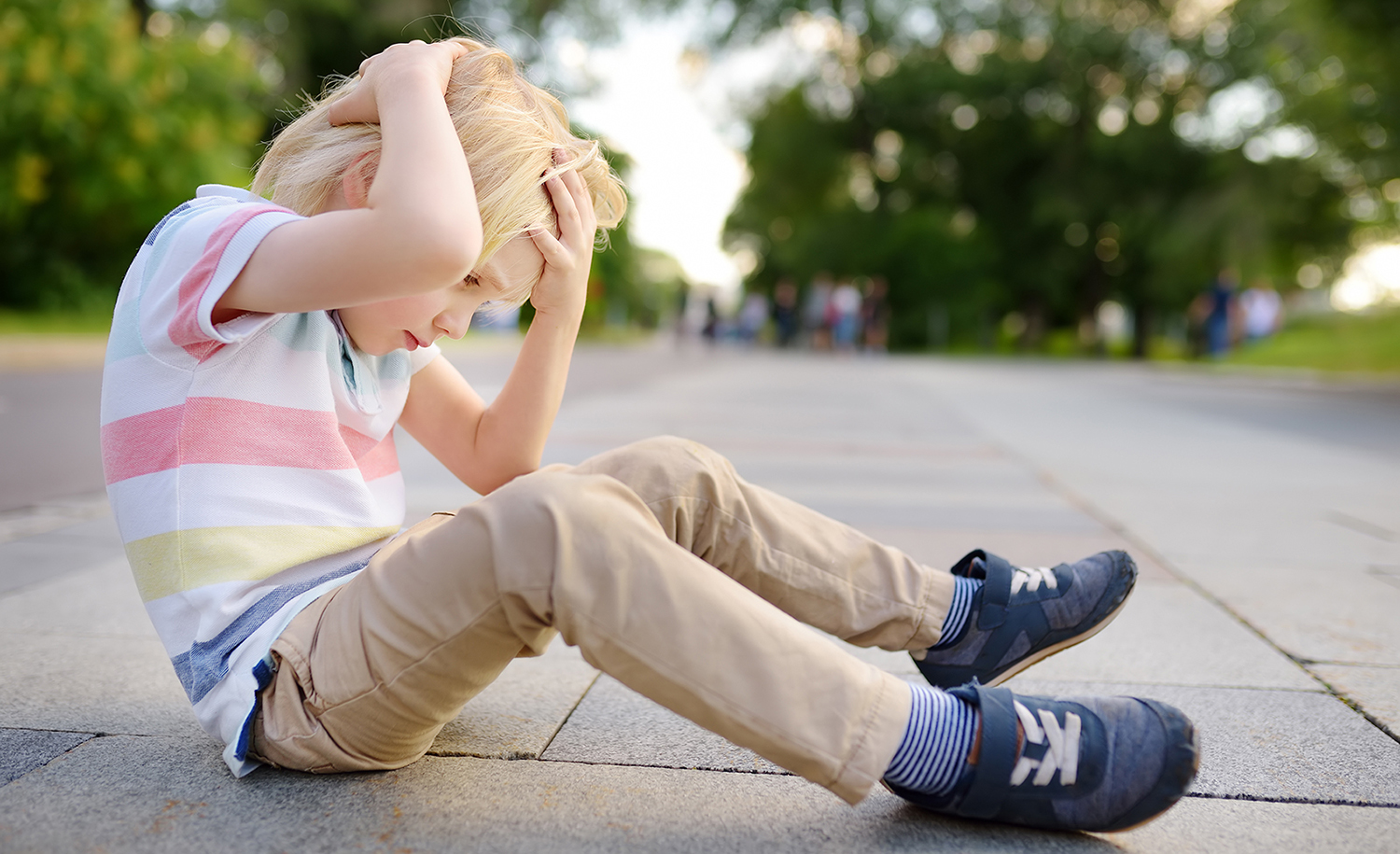 A child sitting on the pavement, holding their head.