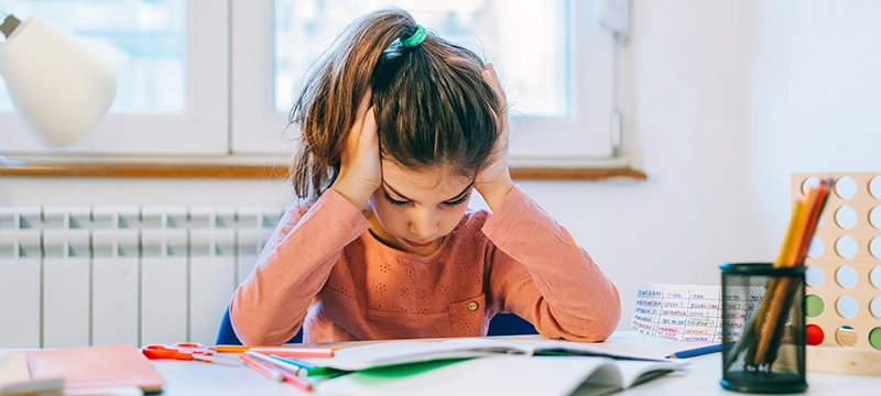 A young girl looks distressed as she tries to focus on her homework, representing executive dysfunction in students and how it can impact academic poerformance