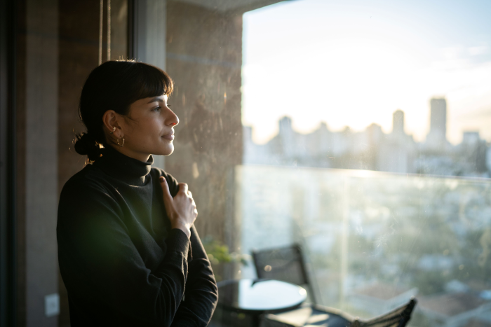 A woman stands by a window looking out thoughtfully