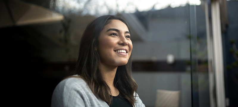 A teen girl smiles while looking out a window, representing positive psychology and overall optimism